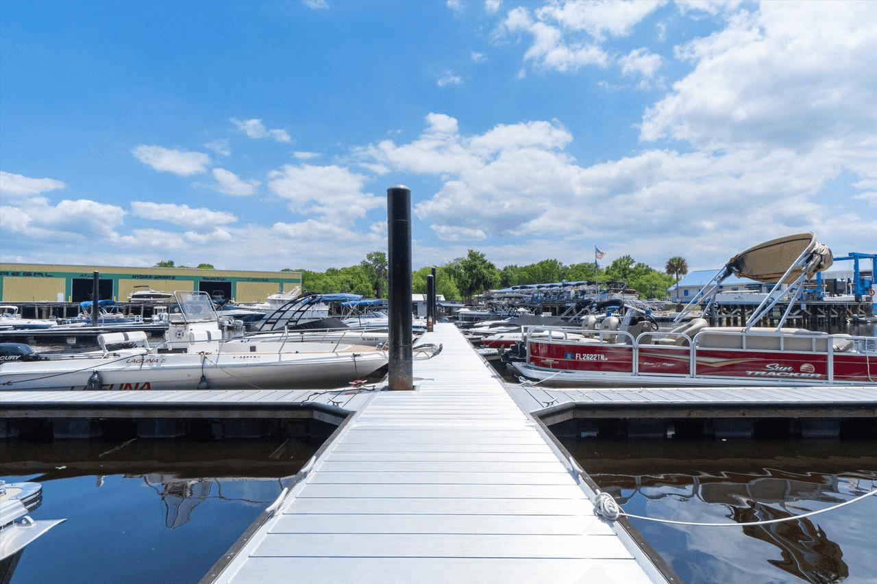Marina dock walkway lined with covered slips and boats on both sides under a bright sky